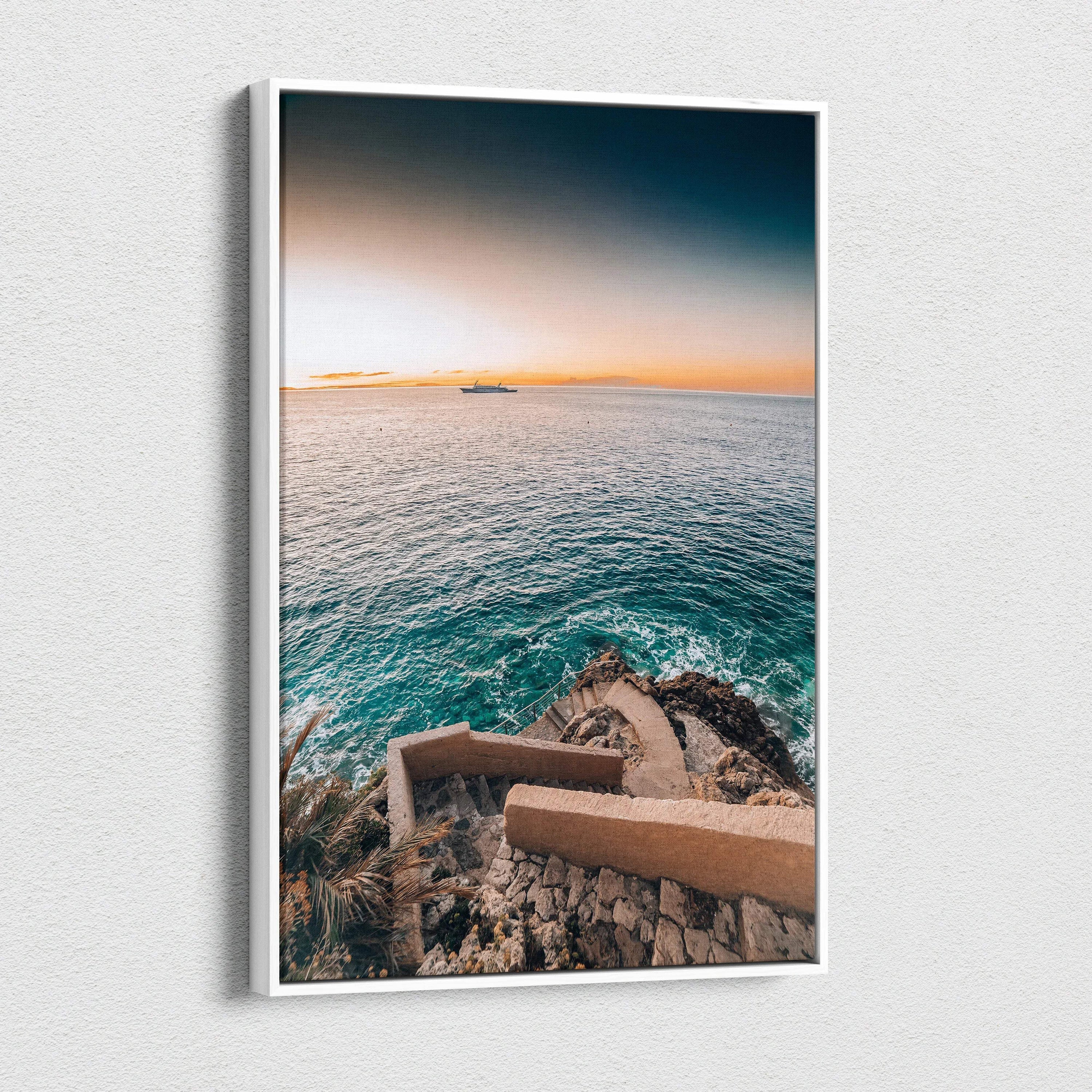 Canvas wall art featuring a serene ocean view with rocky coastline and stairs, warm sunset tones.