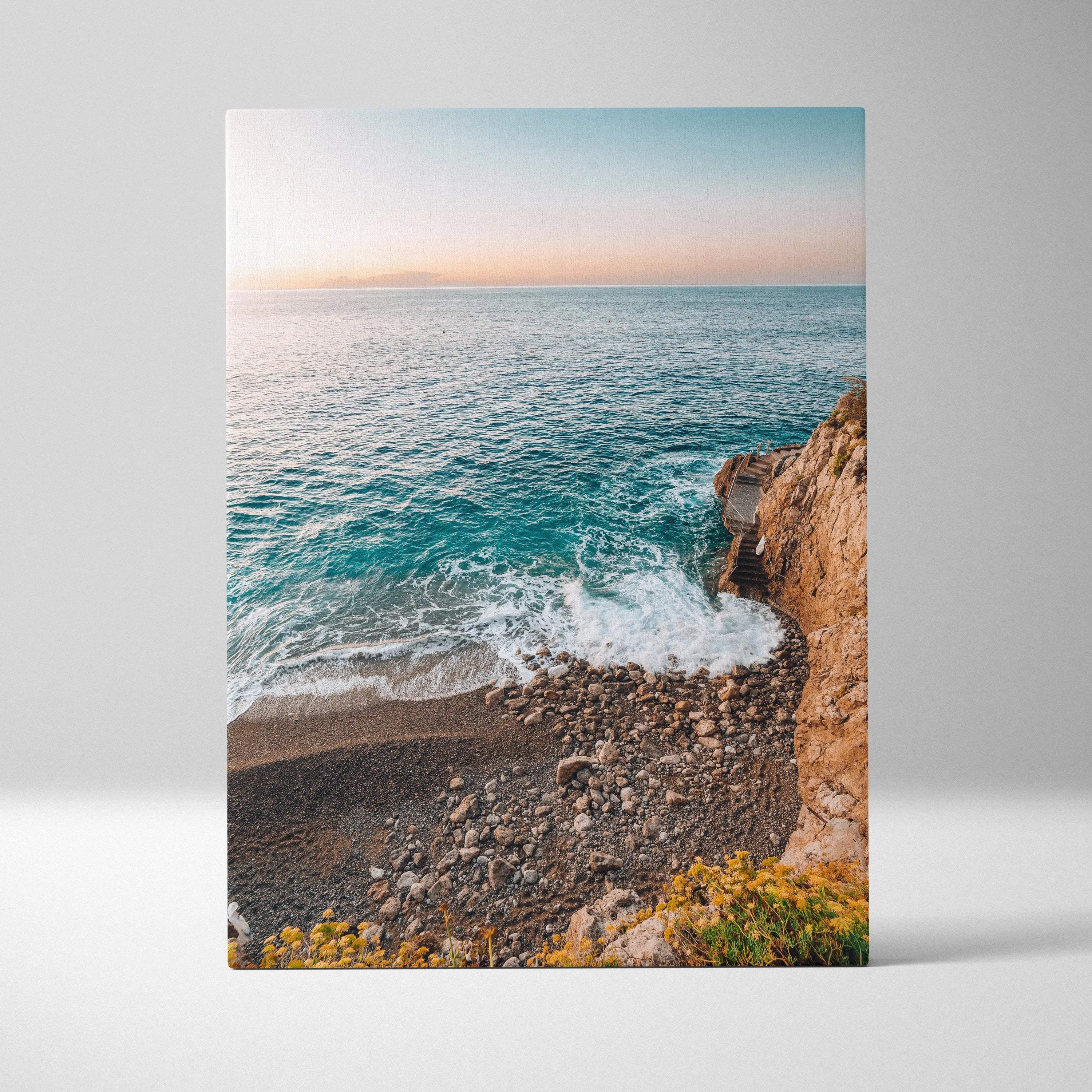 Canvas wall art depicting a serene beach scene with blue ocean waves, rocky shore, and soft pastel sky at sunset.