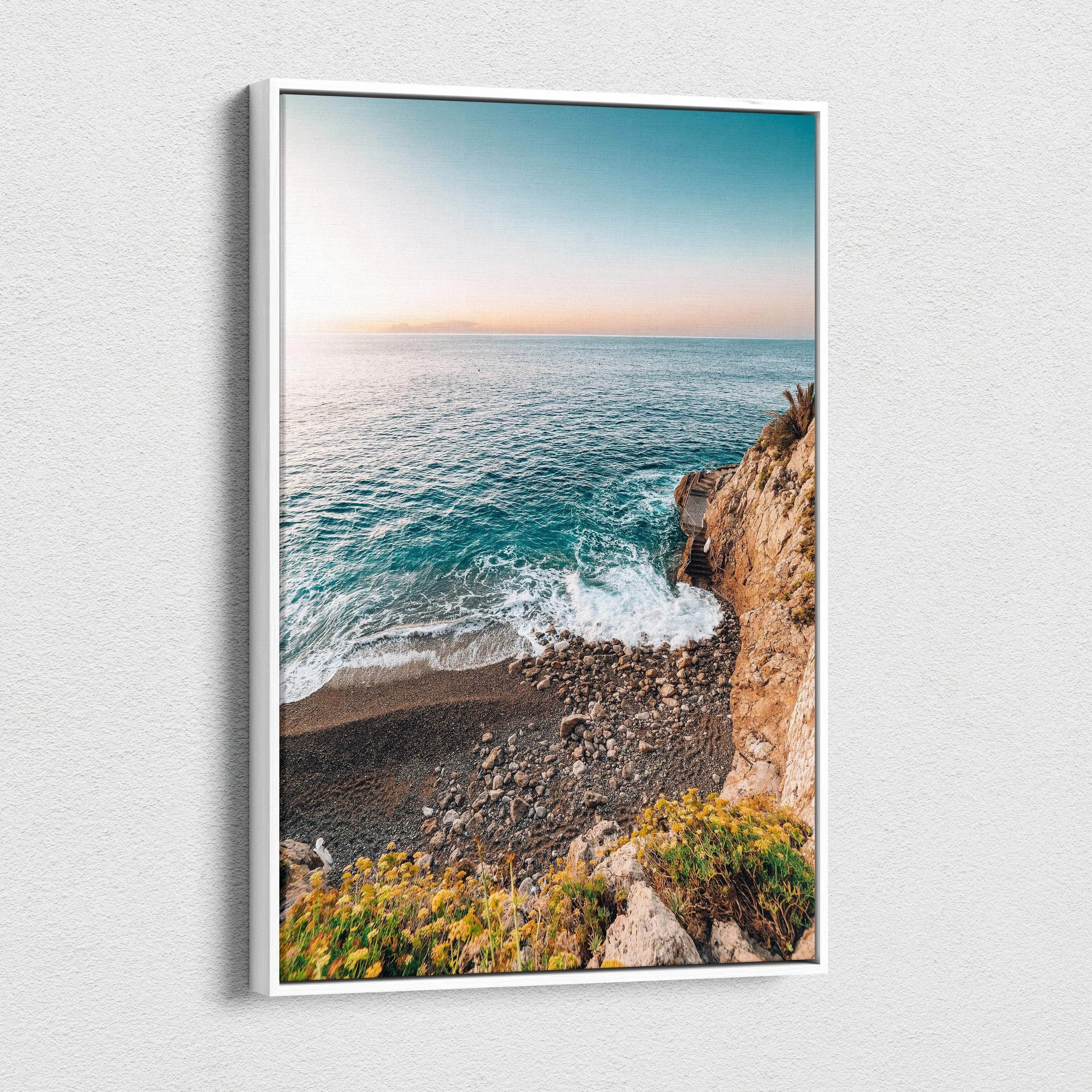 Canvas wall art featuring a tranquil beach scene with blue ocean waves, rocky shore, and sunset sky.