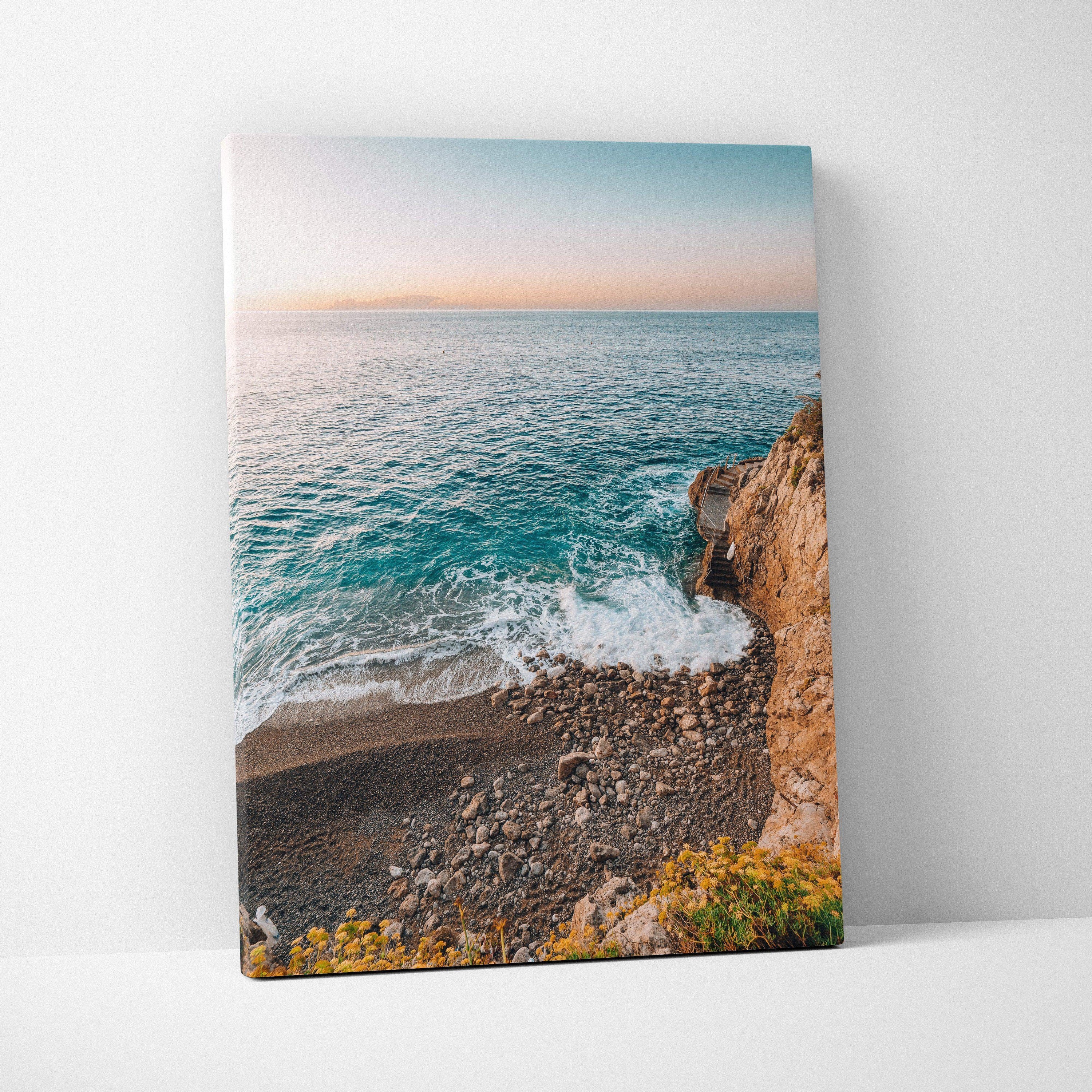 Canvas wall art featuring a serene beach scene with blue ocean waves, rocky shore, and soft pastel sky.
