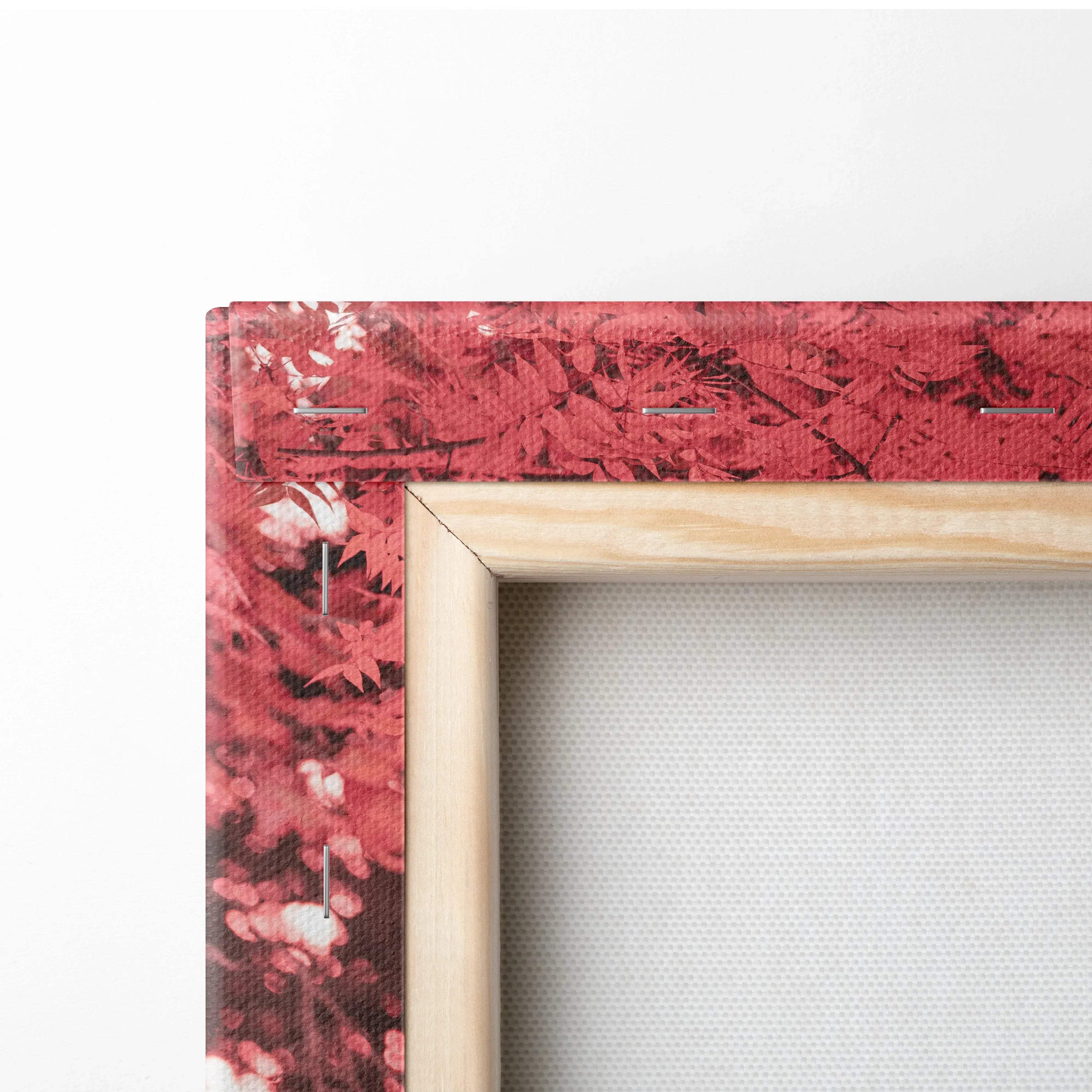 Close-up of wooden frame corner and textured red canvas wall art with leaf pattern.