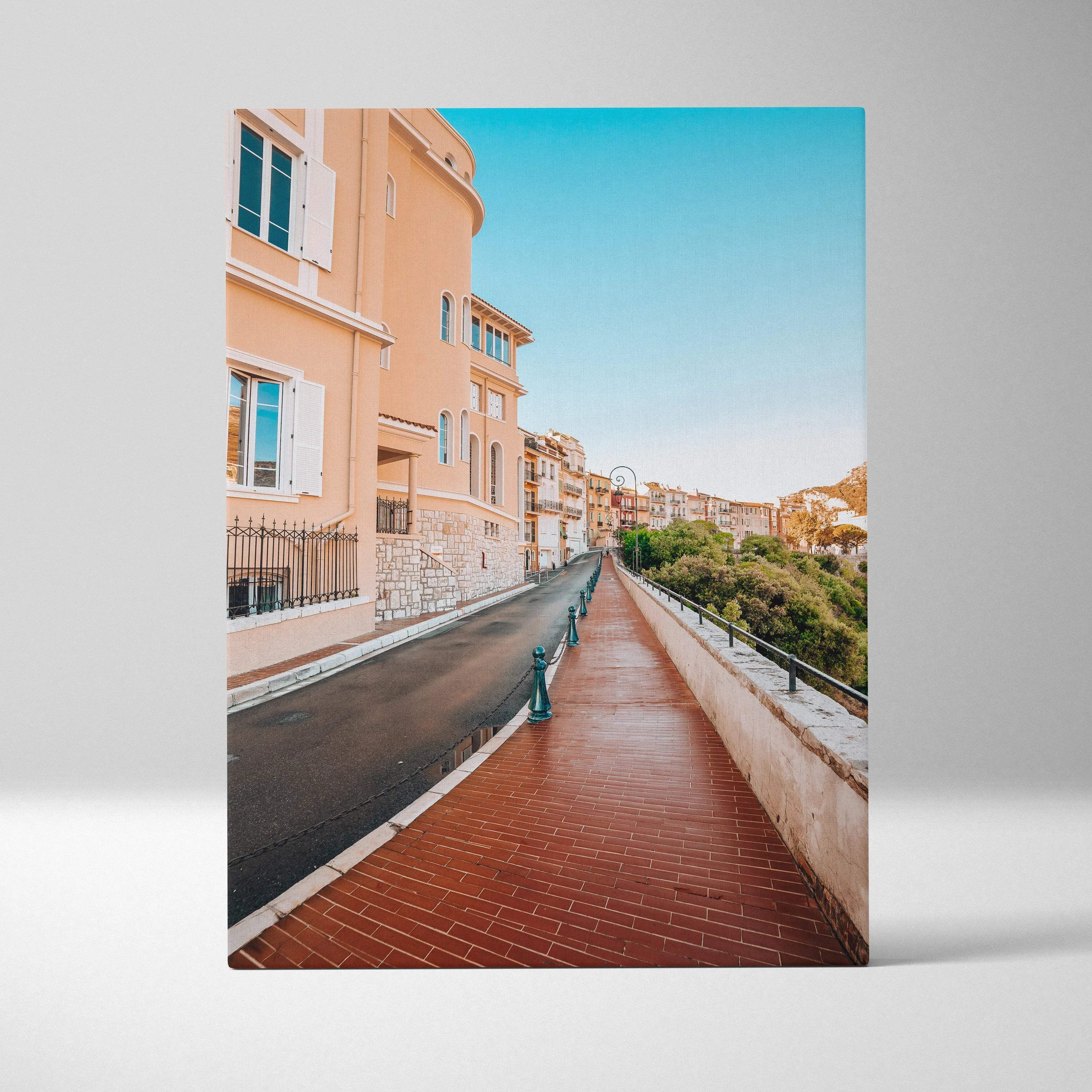 A rectangular canvas print showing a sunlit european street with peach buildings red brick pavement and clear blue sky