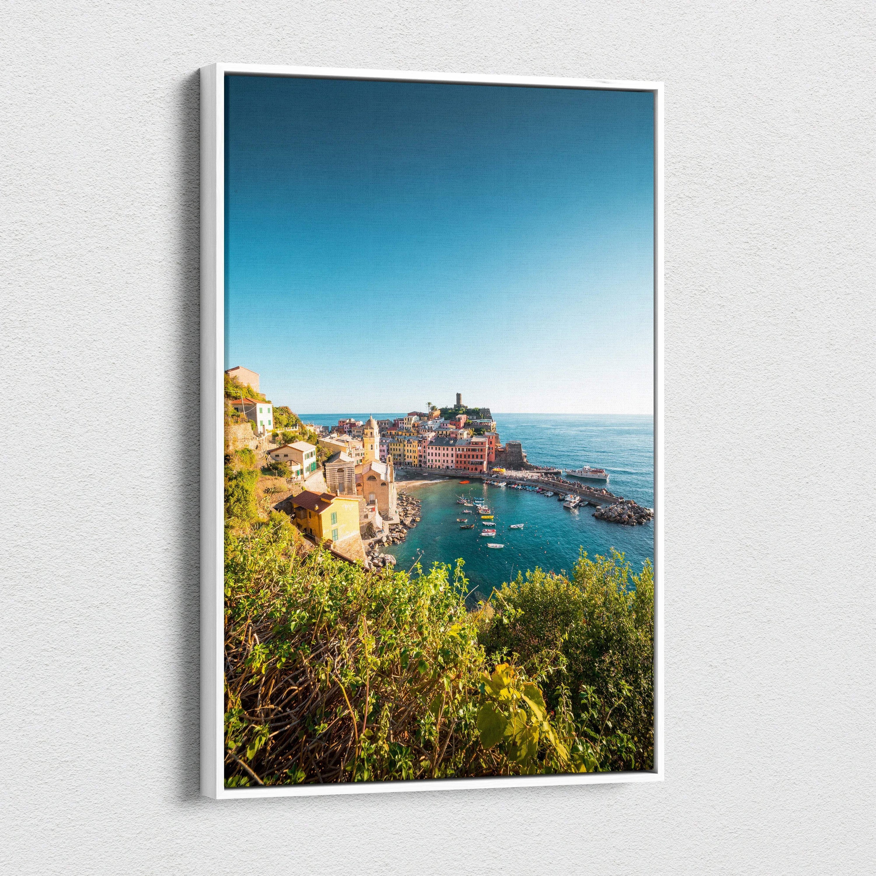 Vertical canvas wall art featuring vibrant coastal architecture under a clear blue sky with lush greenery in the foreground.