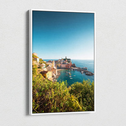 Vertical canvas wall art featuring vibrant coastal architecture under a clear blue sky with lush greenery in the foreground.