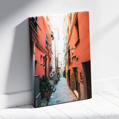 Vertical canvas wall art featuring vibrant architectural alleyway with orange buildings and narrow street.