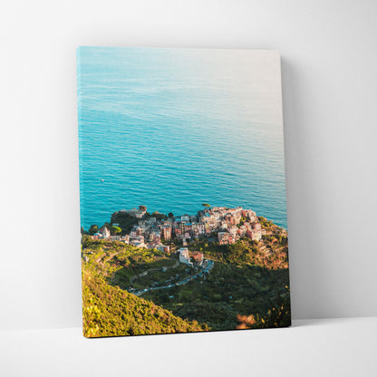 Canvas wall art featuring a coastal village with terracotta roofs beside calm blue ocean waters.