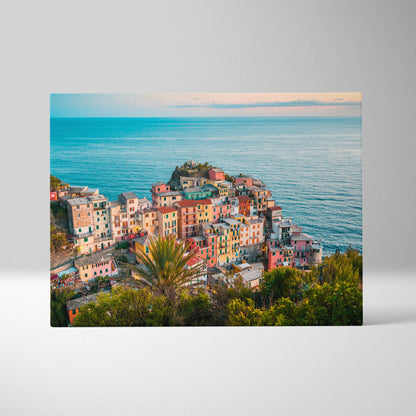 Canvas wall art showcasing colorful coastal buildings clustered on a hillside by a calm blue ocean at sunset.