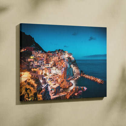 Oceanfront village illuminated at dusk on canvas wall art with vibrant blue sky and glowing buildings.