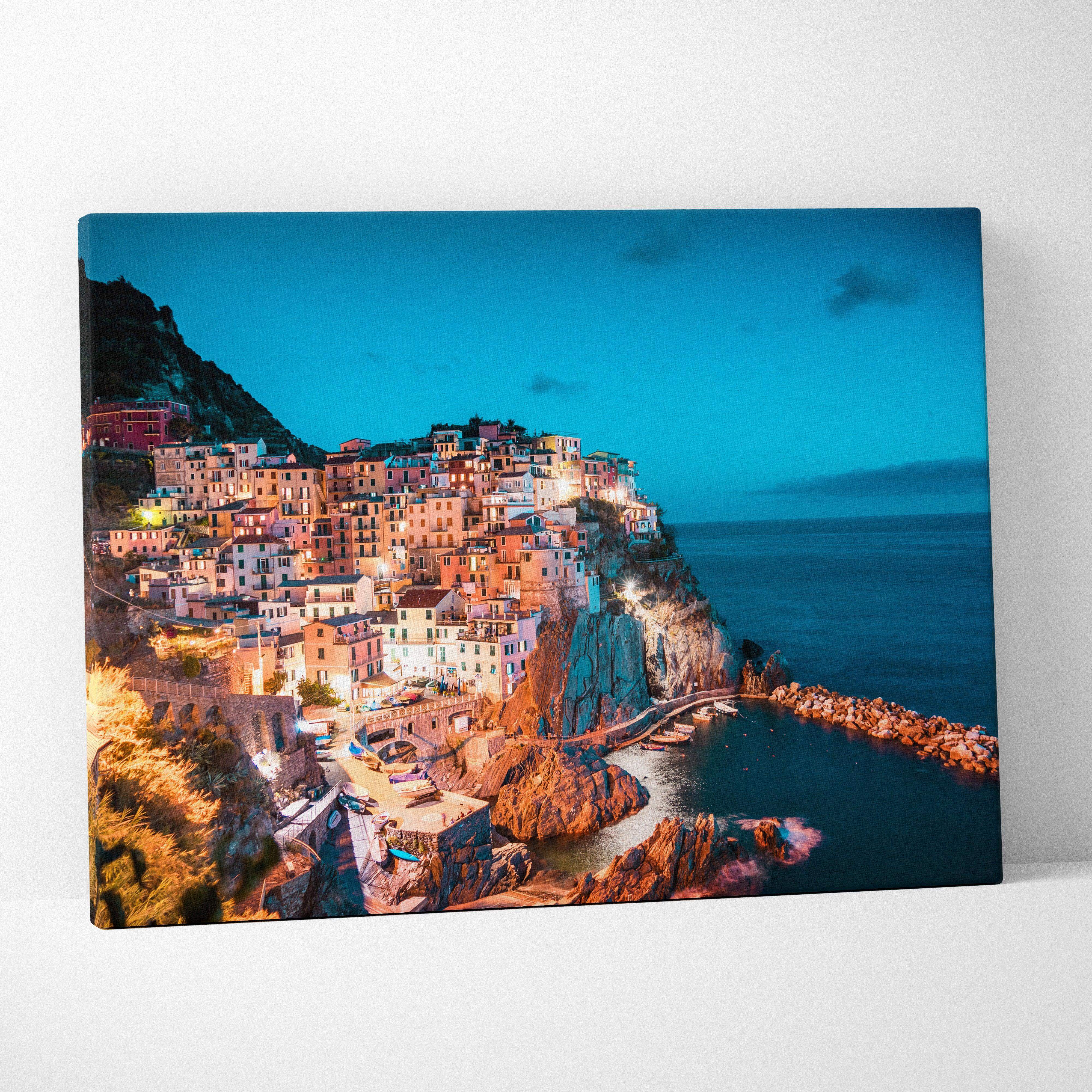 A vibrant coastal townscape canvas wall art depicting a dusk cliffside village by the ocean in iridescent blue tones