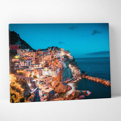 Canvas wall art featuring vibrant coastal buildings on steep cliffs under a deep blue twilight sky.