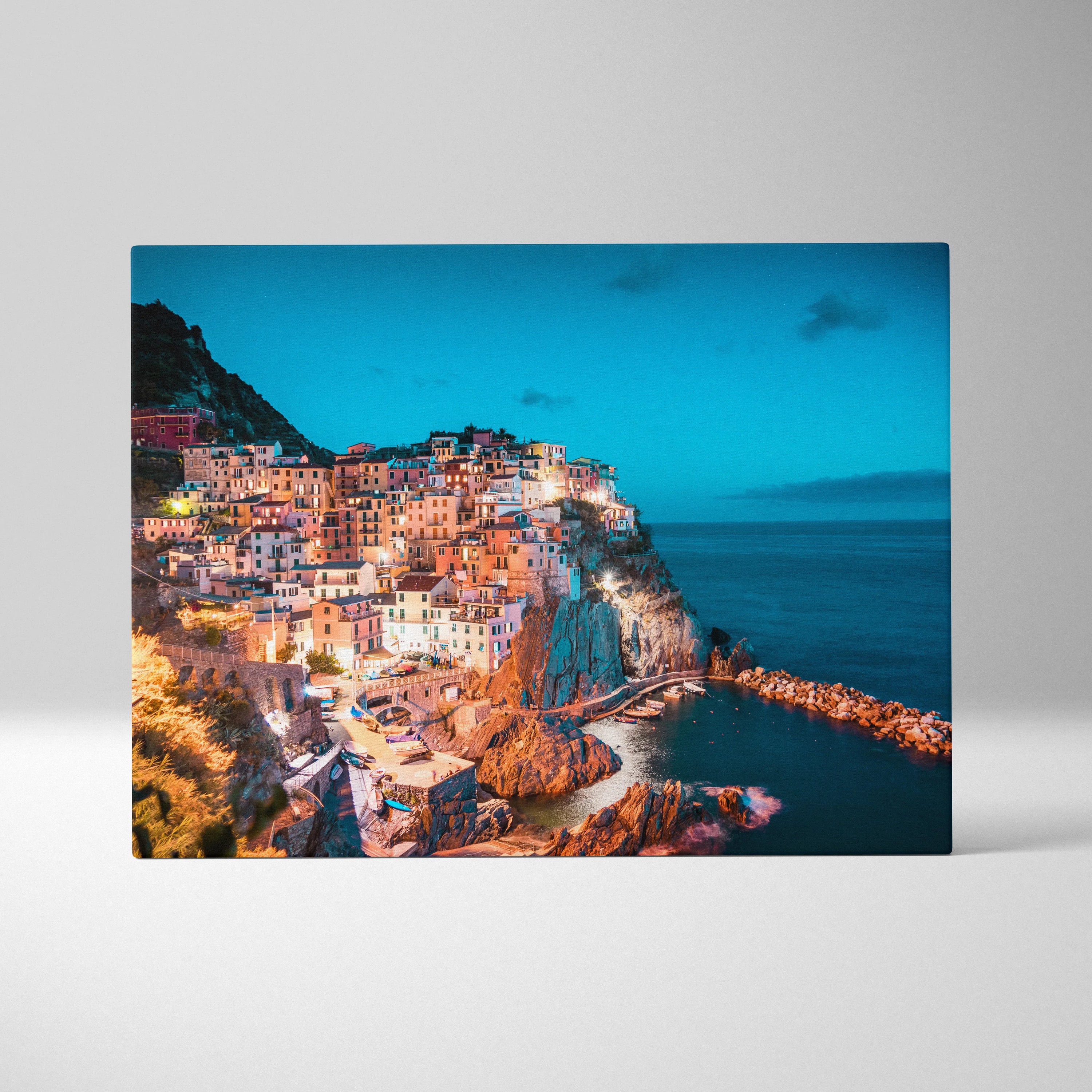 Canvas wall art featuring a vibrant coastal village at dusk with illuminated buildings and deep blue ocean.