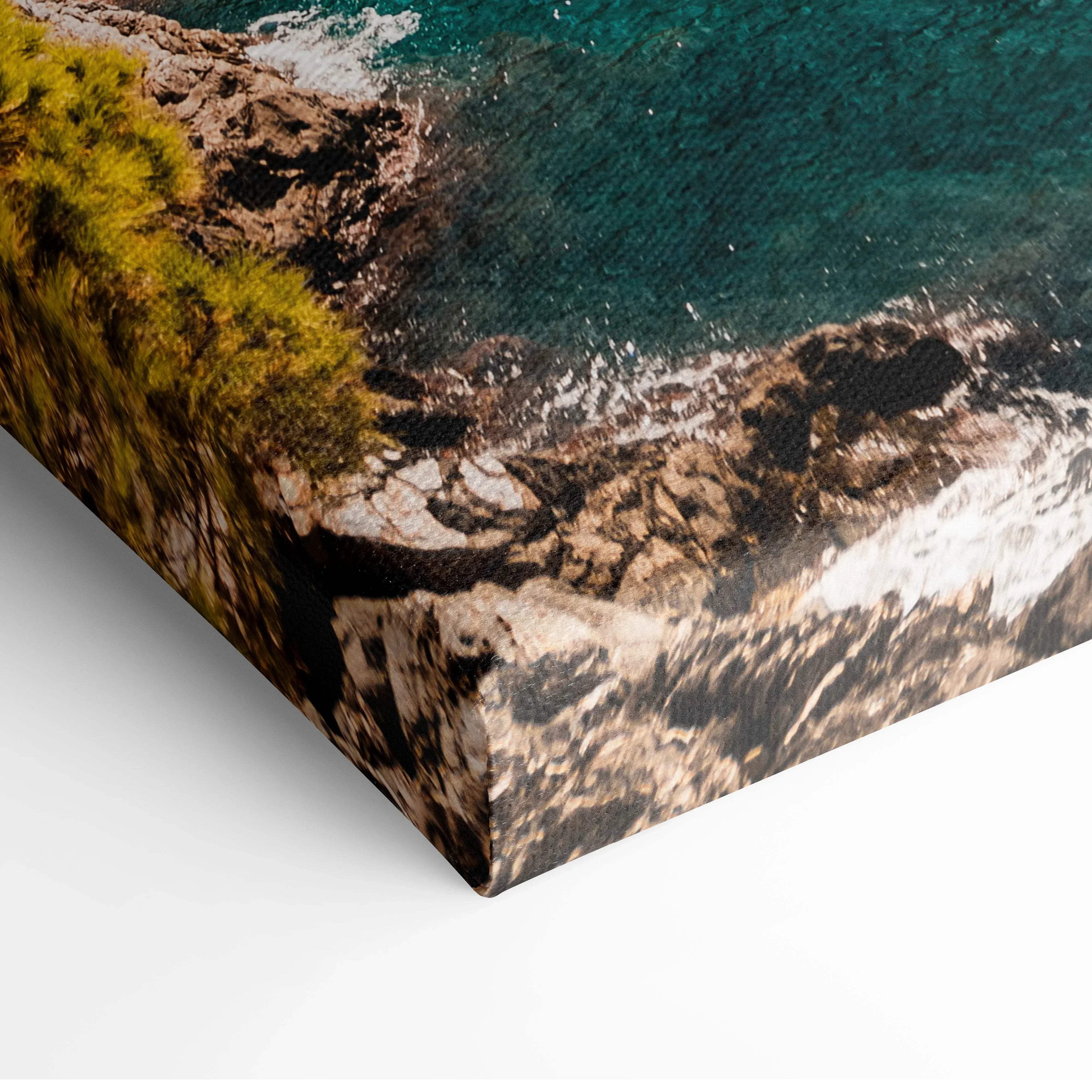 Close-up of canvas wall art showing textured rocky coastline and blue water with green trees in digital style.