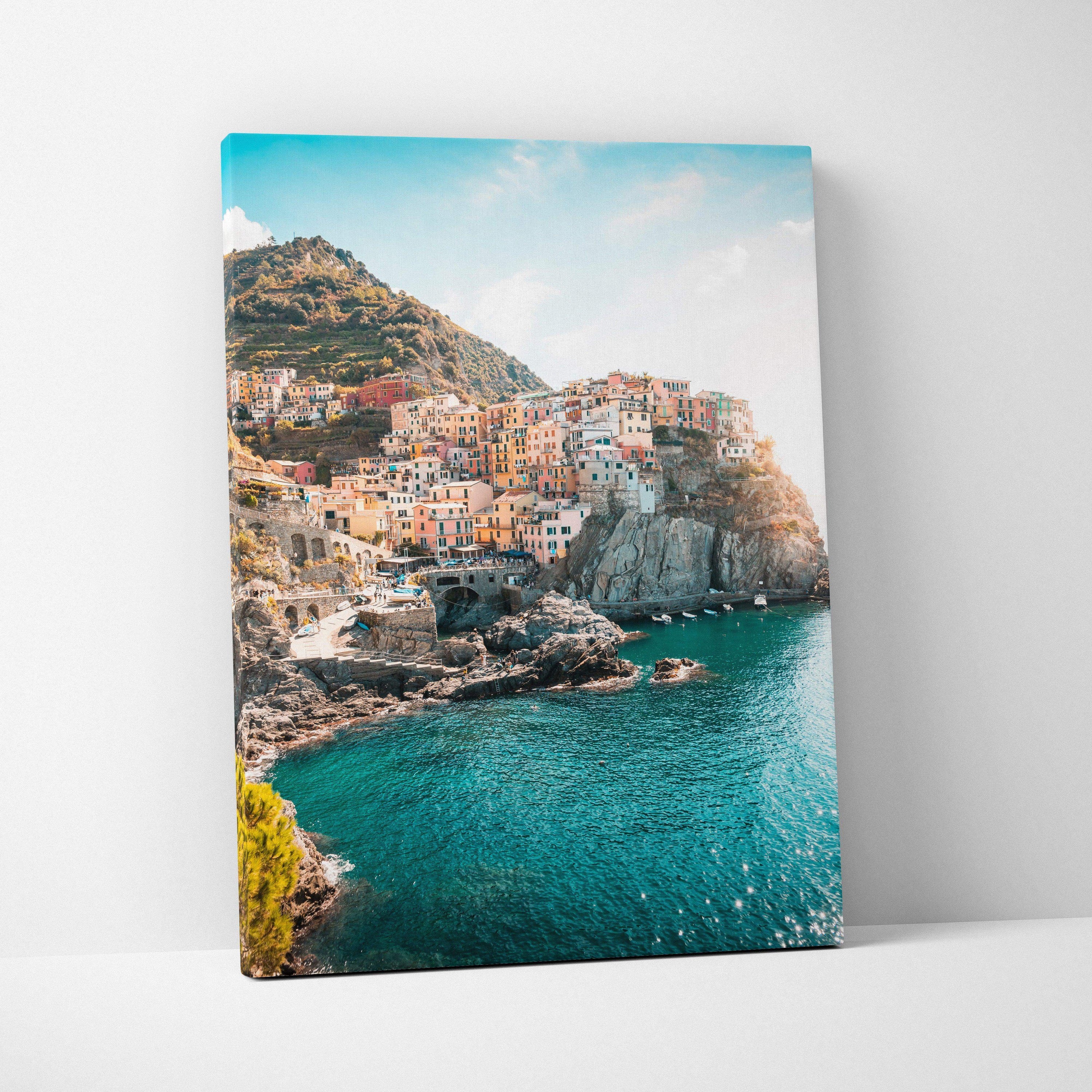Canvas wall art depicting colorful coastal buildings on rocky cliffs beside turquoise water under a bright sky.