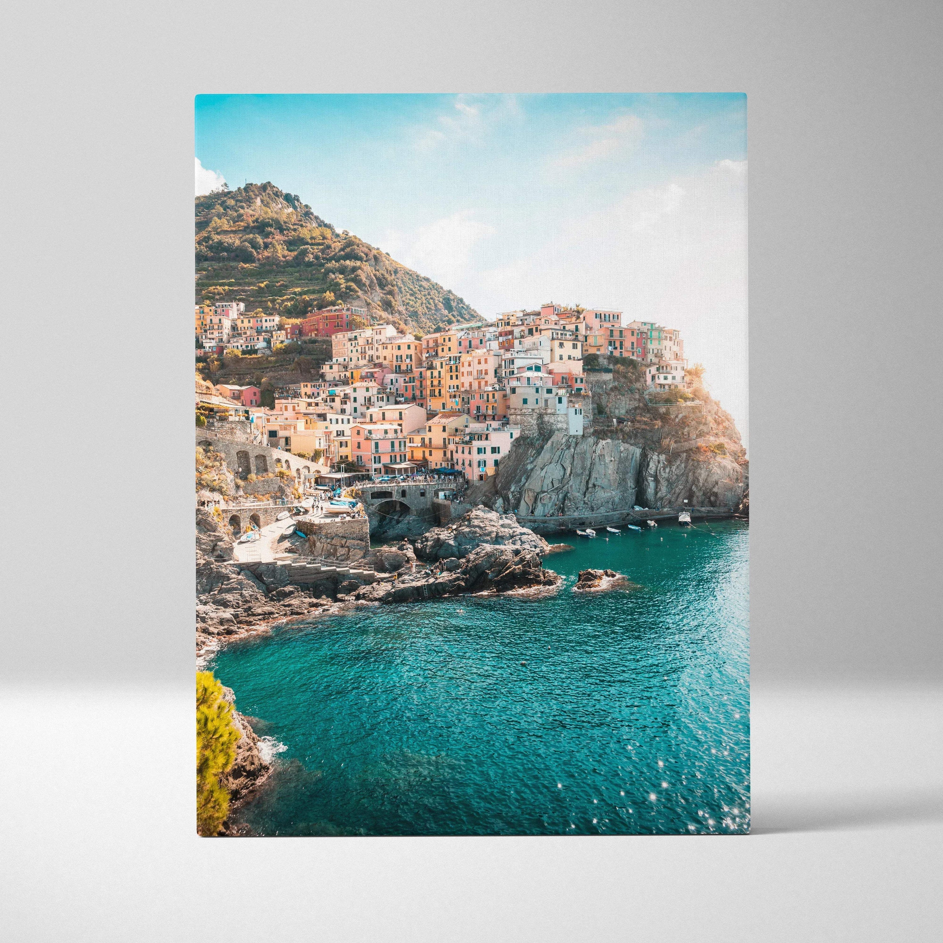 Canvas wall art featuring colorful coastal buildings on rocky cliffs with bright blue water beneath.
