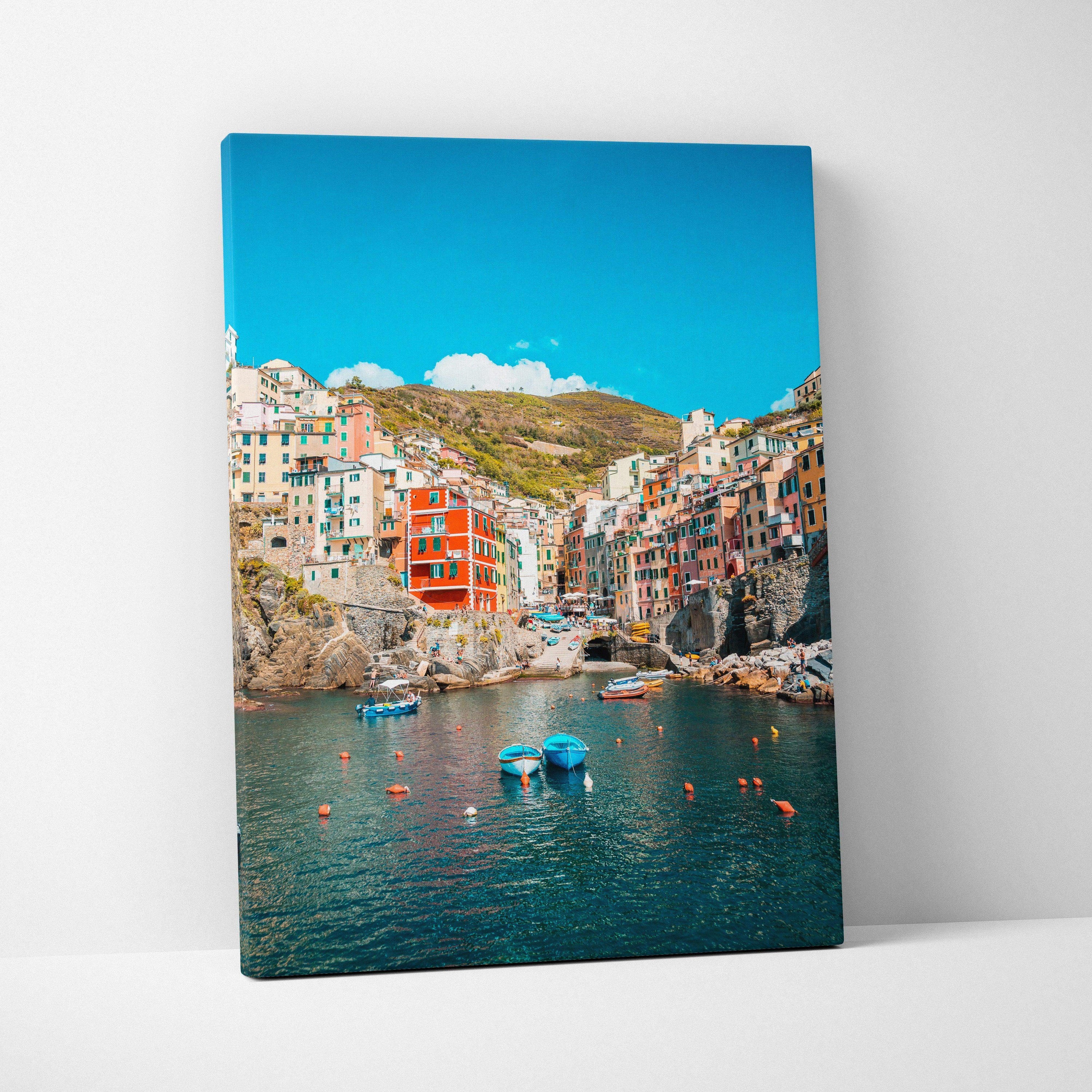 Canvas wall art featuring colorful coastal buildings and clear blue sky over calm harbor water.