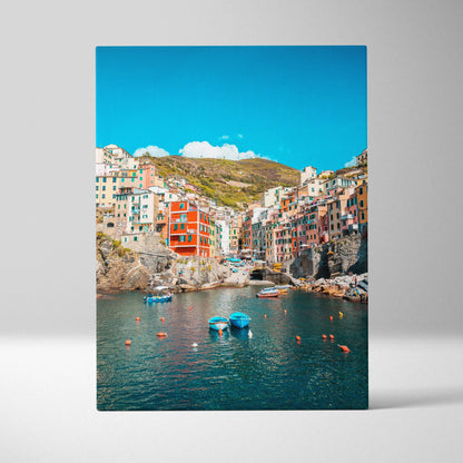 Canvas art wall art featuring colorful hillside buildings overlooking a calm blue harbor with boats under a bright sky.