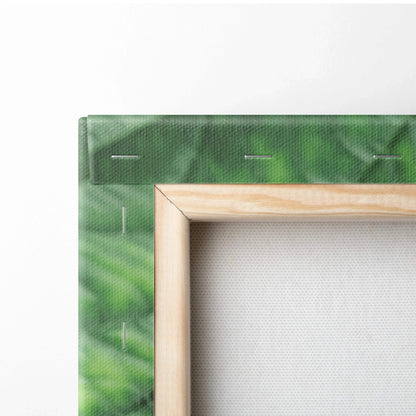 Close-up of wooden frame with green leaf-patterned canvas stretched and stapled for wall art decor.