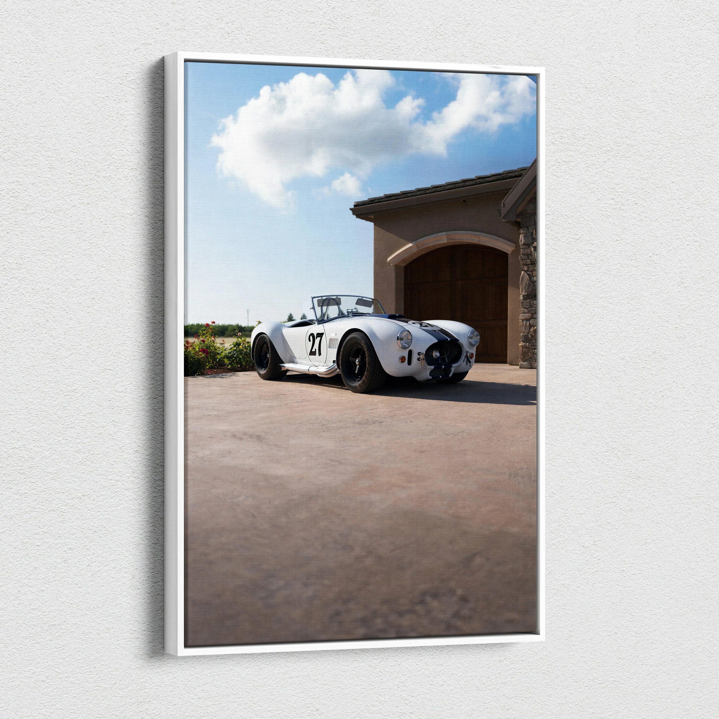 Vertical canvas wall art featuring a classic white Shelby Cobra parked outside a garage under a blue sky with clouds.