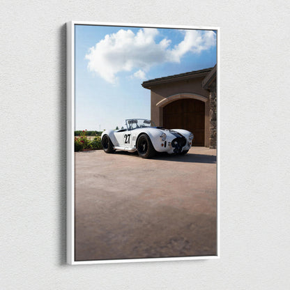 Vertical canvas wall art featuring a classic white Shelby Cobra parked outside a garage under a blue sky with clouds.