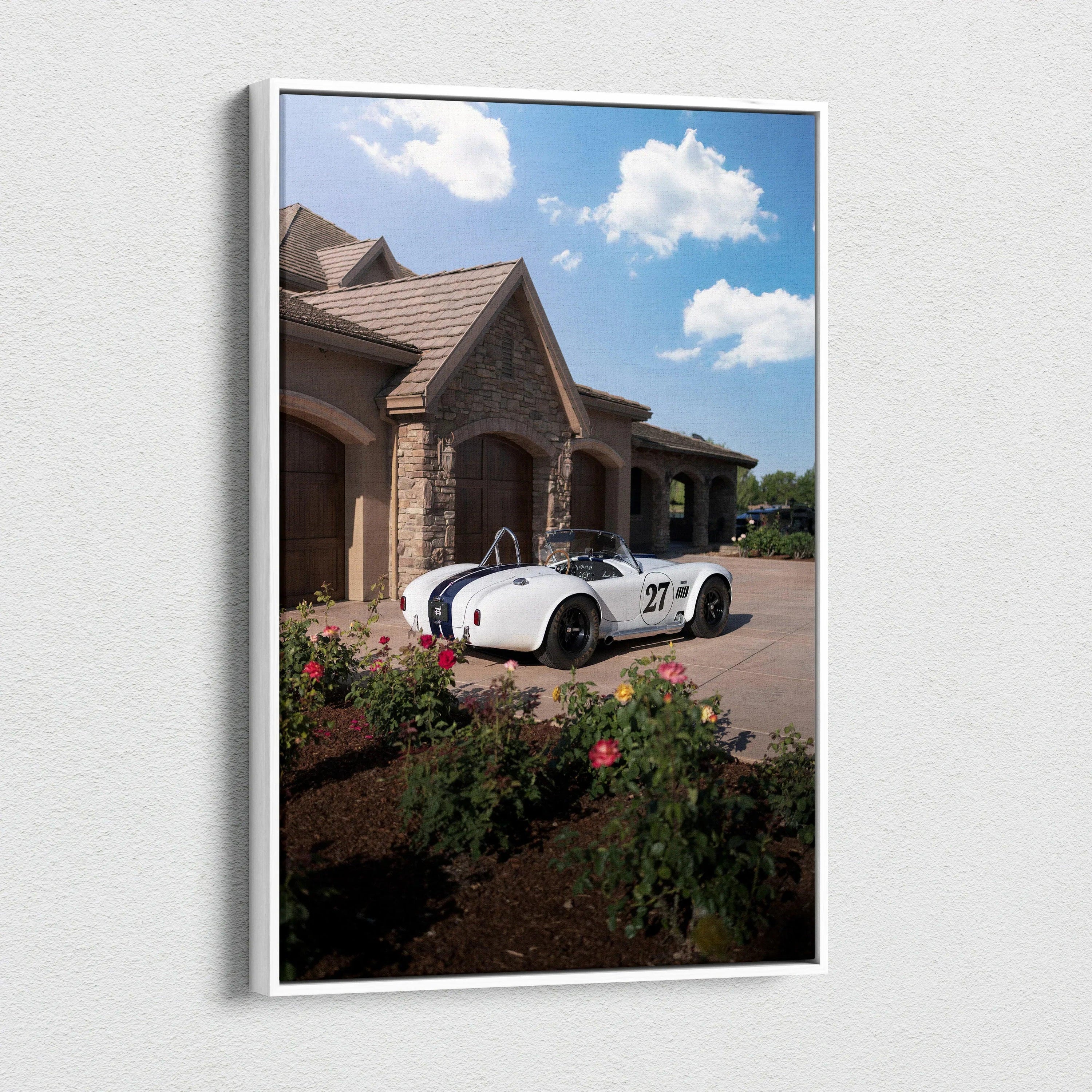 Vertical canvas art of white Shelby Cobra sports car parked by stone house under blue sky with clouds.