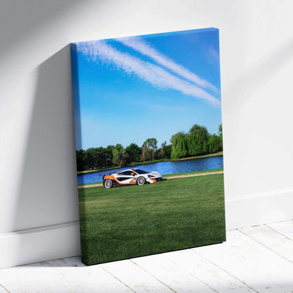 Vertical canvas wall art featuring a McLaren 570S sports car on green grass by a lake under a blue sky.