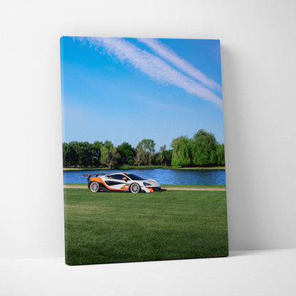 Vertical canvas wall art featuring a McLaren 570S on green grass with a lake and blue sky background.