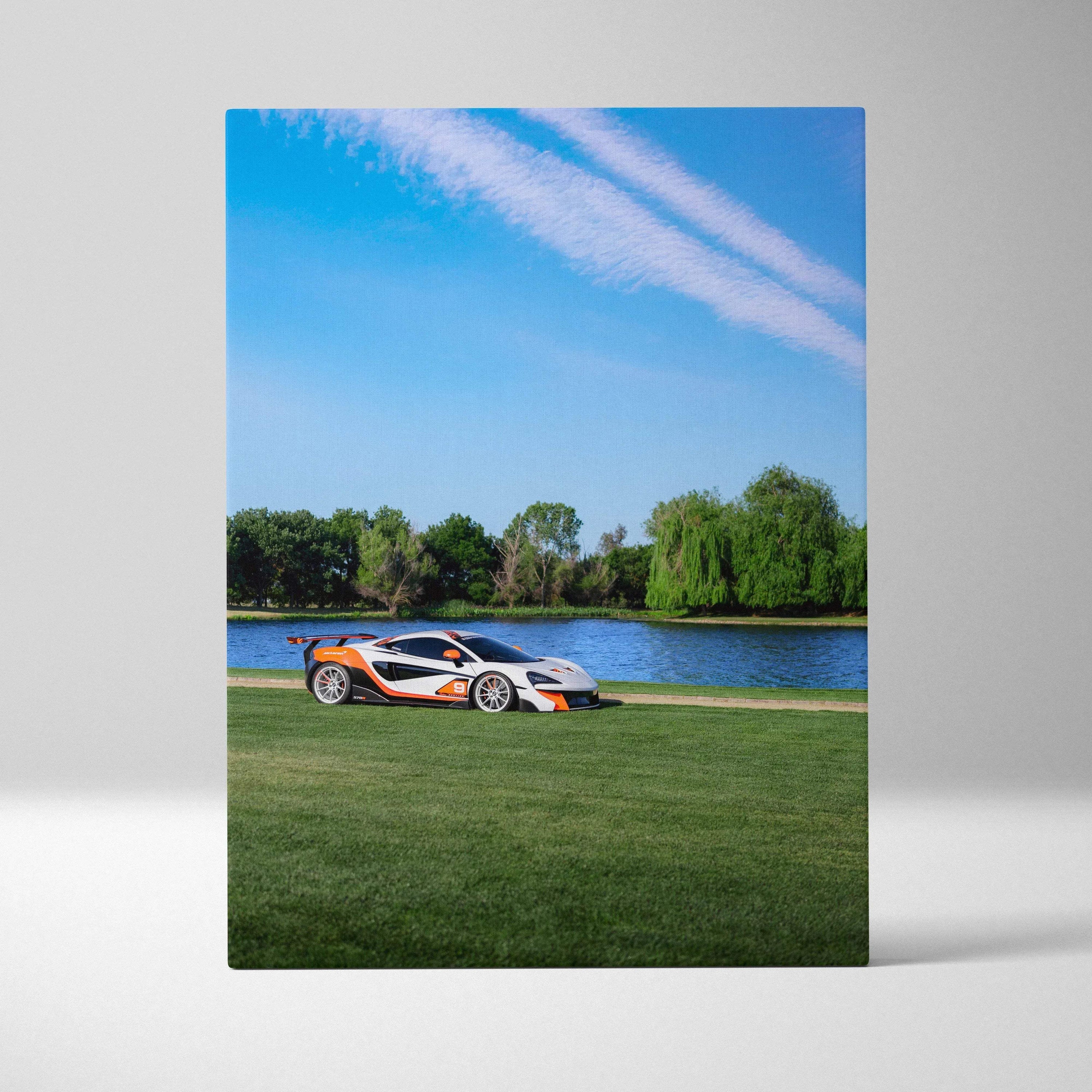 Vertical canvas art of a white and orange McLaren 570S car on green grass by a lake under blue sky.