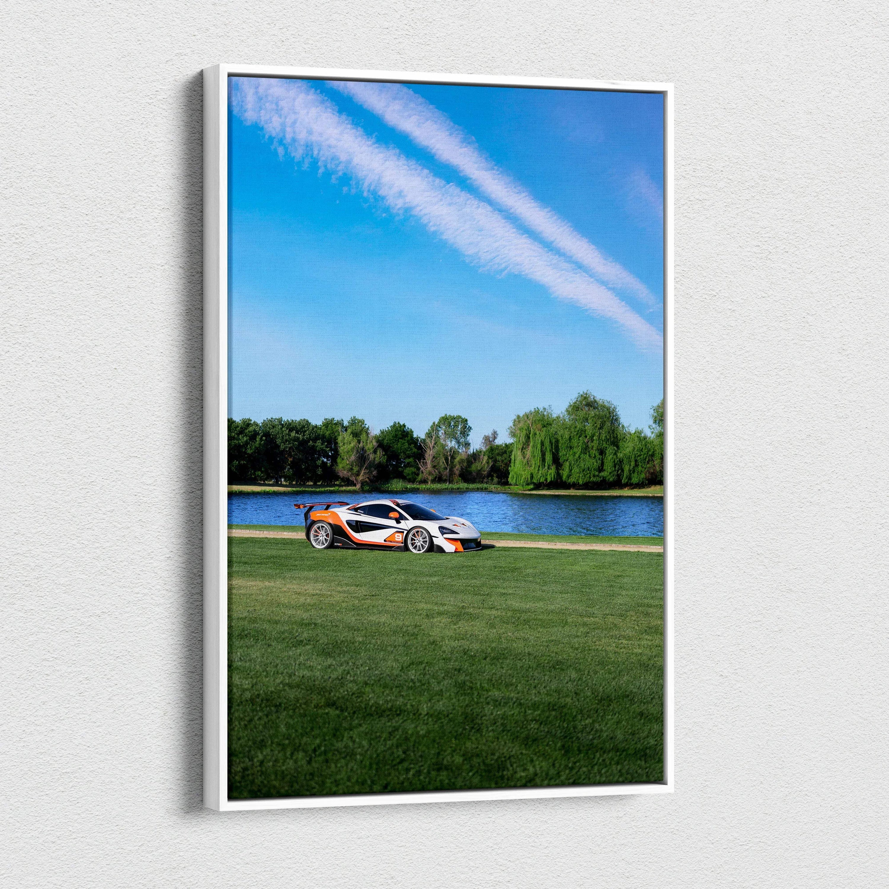 Vertical canvas wall art featuring a McLaren 570S on green grass by a lake under a blue sky.