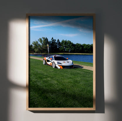 McLaren 570S sports car on grass by lake with blue sky, high-resolution poster wall art.
