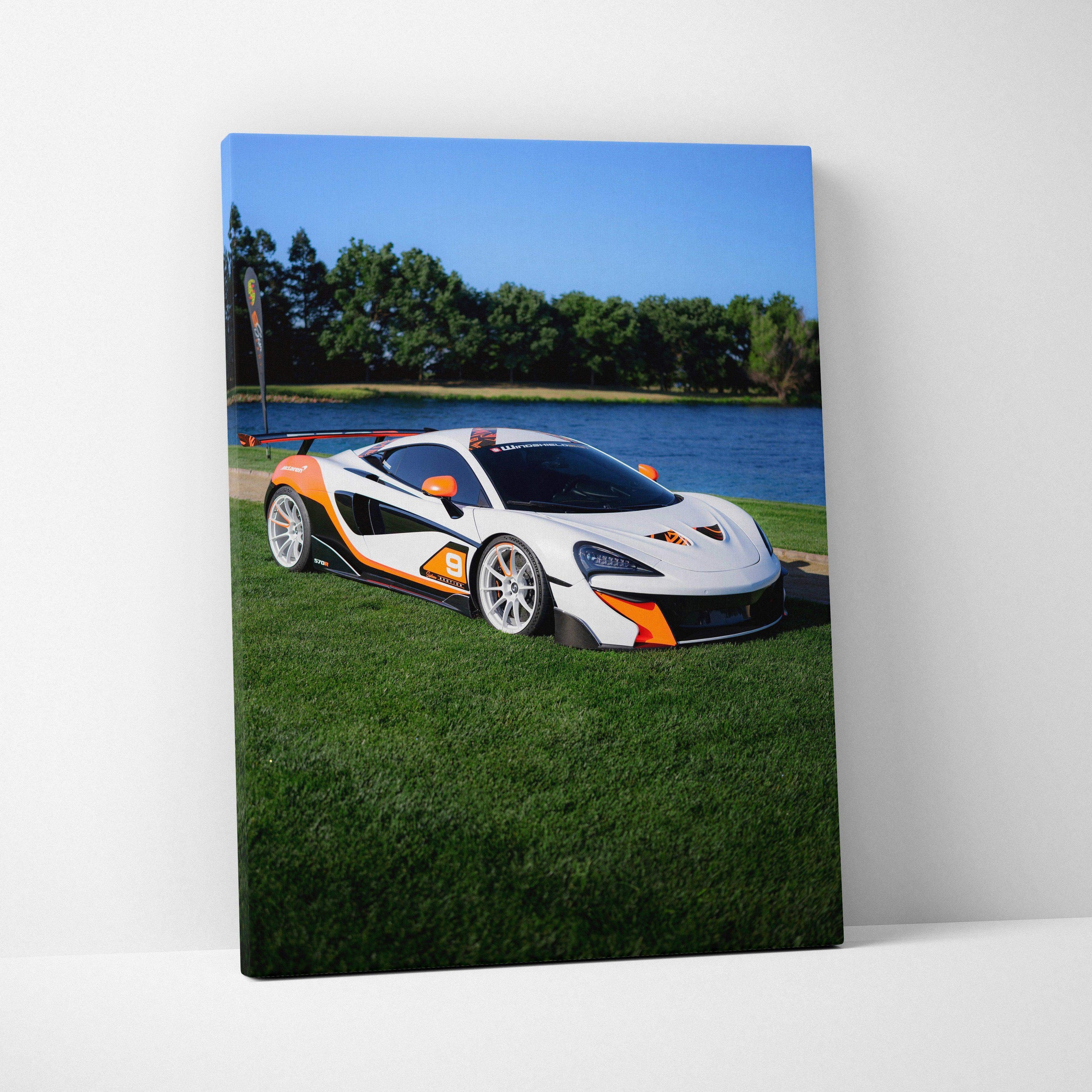 Vertical canvas wall art featuring a white McLaren 570S with orange accents on grass by a lake.