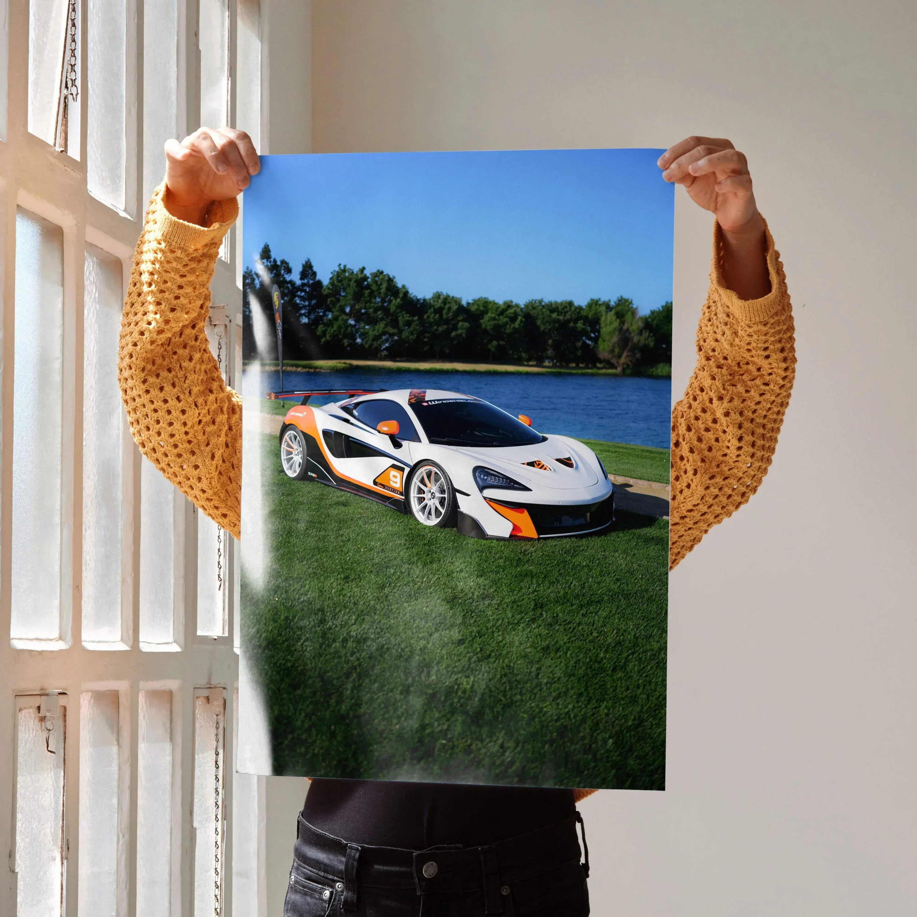 McLaren 570S poster showing white and orange sports car on green grass near water, wall art with vibrant colors.