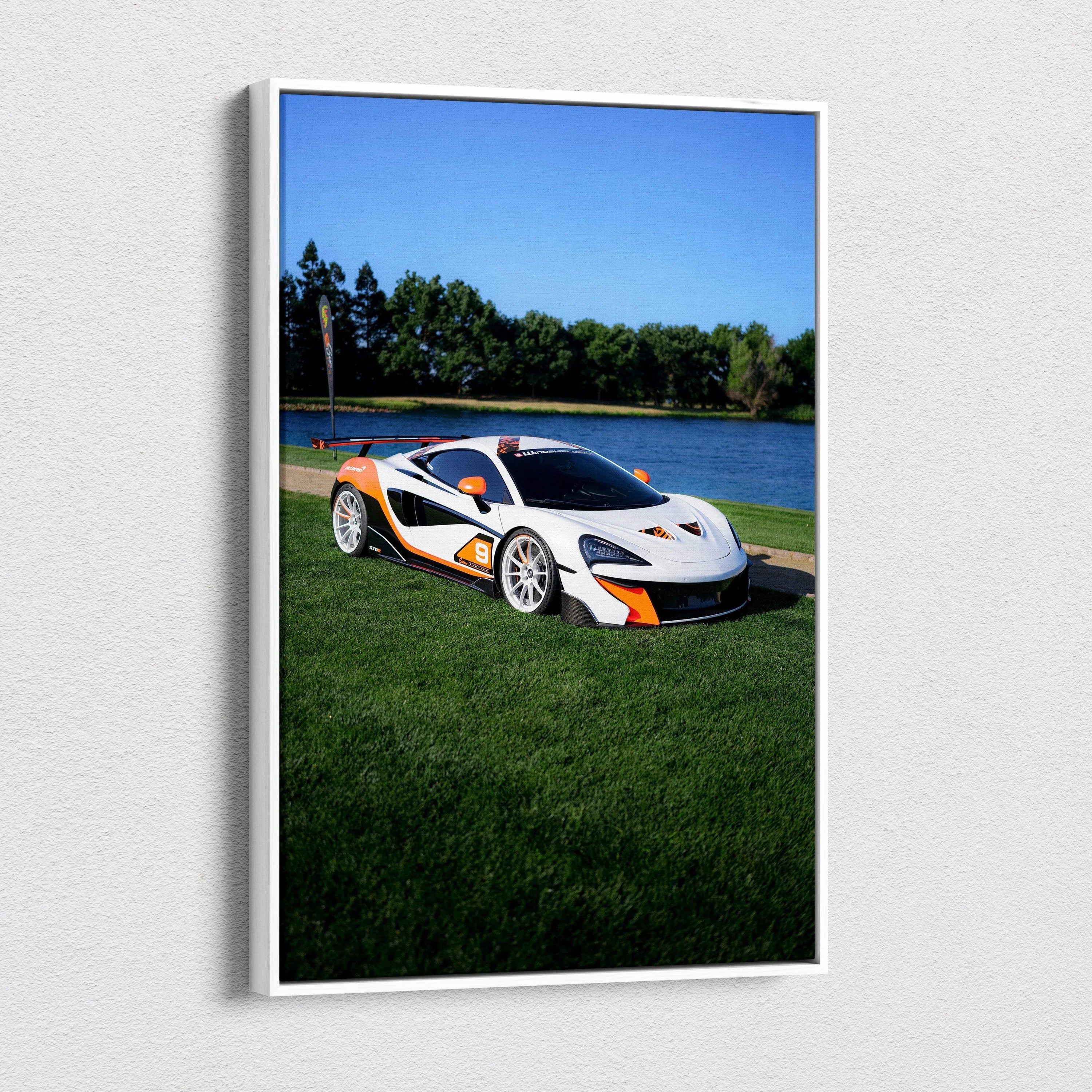 Vertical canvas wall art featuring a white McLaren 570S with orange accents on green grass by a lake.