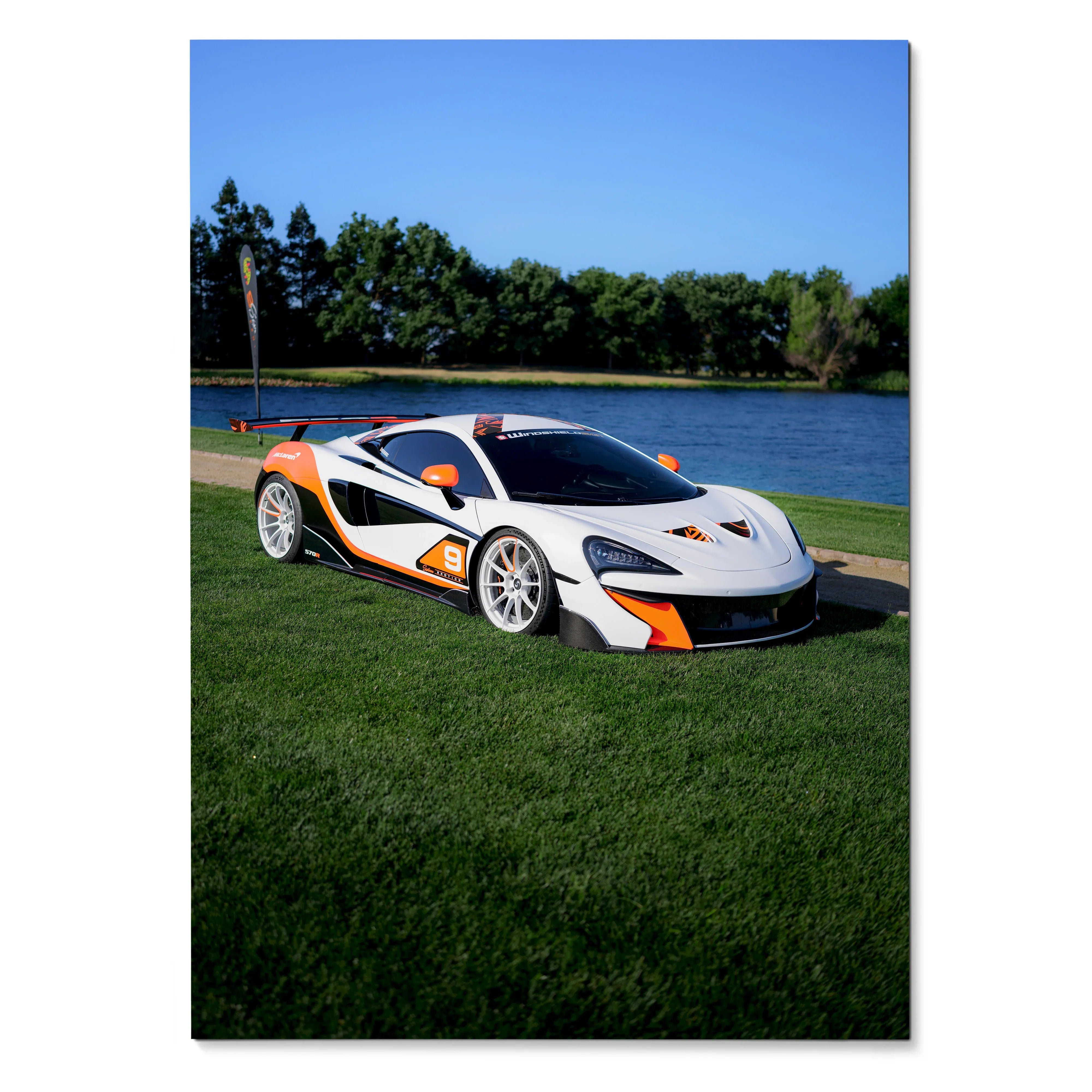 McLaren 570S sports car parked on green grass by water under clear blue sky poster wall art.