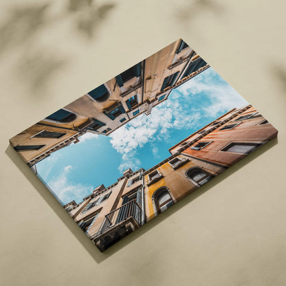 Premium canvas wall art featuring upward view of colorful architecture under blue sky with clouds.