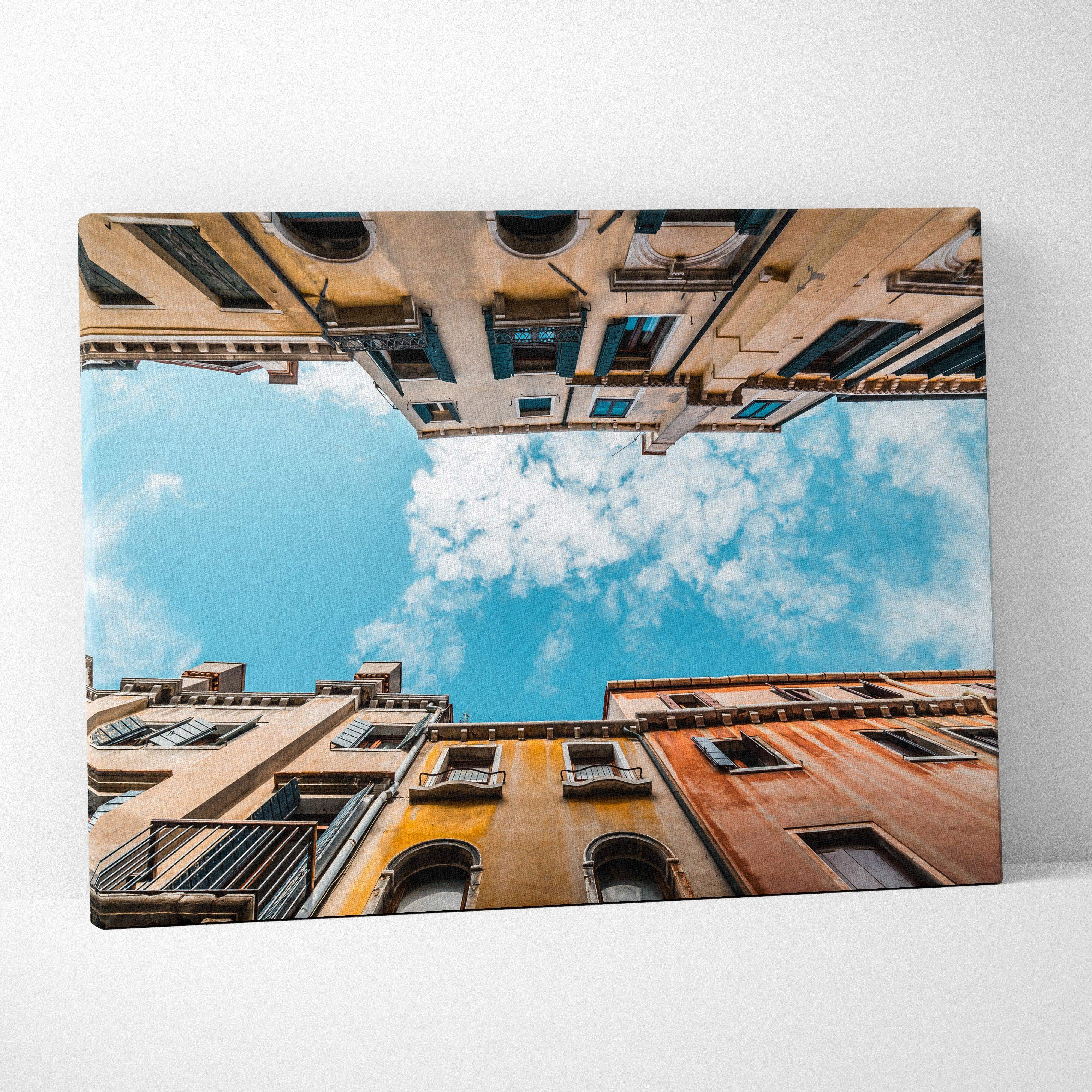 A vibrant canvas wall art featuring low-angle historic european building facades with blue shutters and bright sky