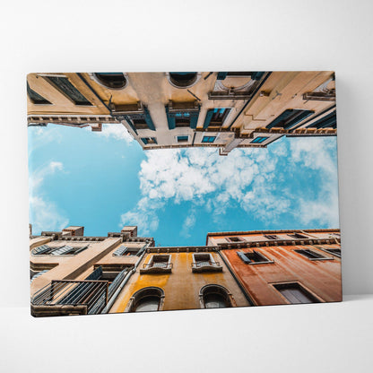Canvas wall art featuring an upward view of colorful Mediterranean buildings against a bright blue sky with scattered clouds.