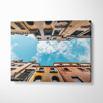 Canvas wall art showing upward view of tall, historic buildings against a blue sky with clouds.