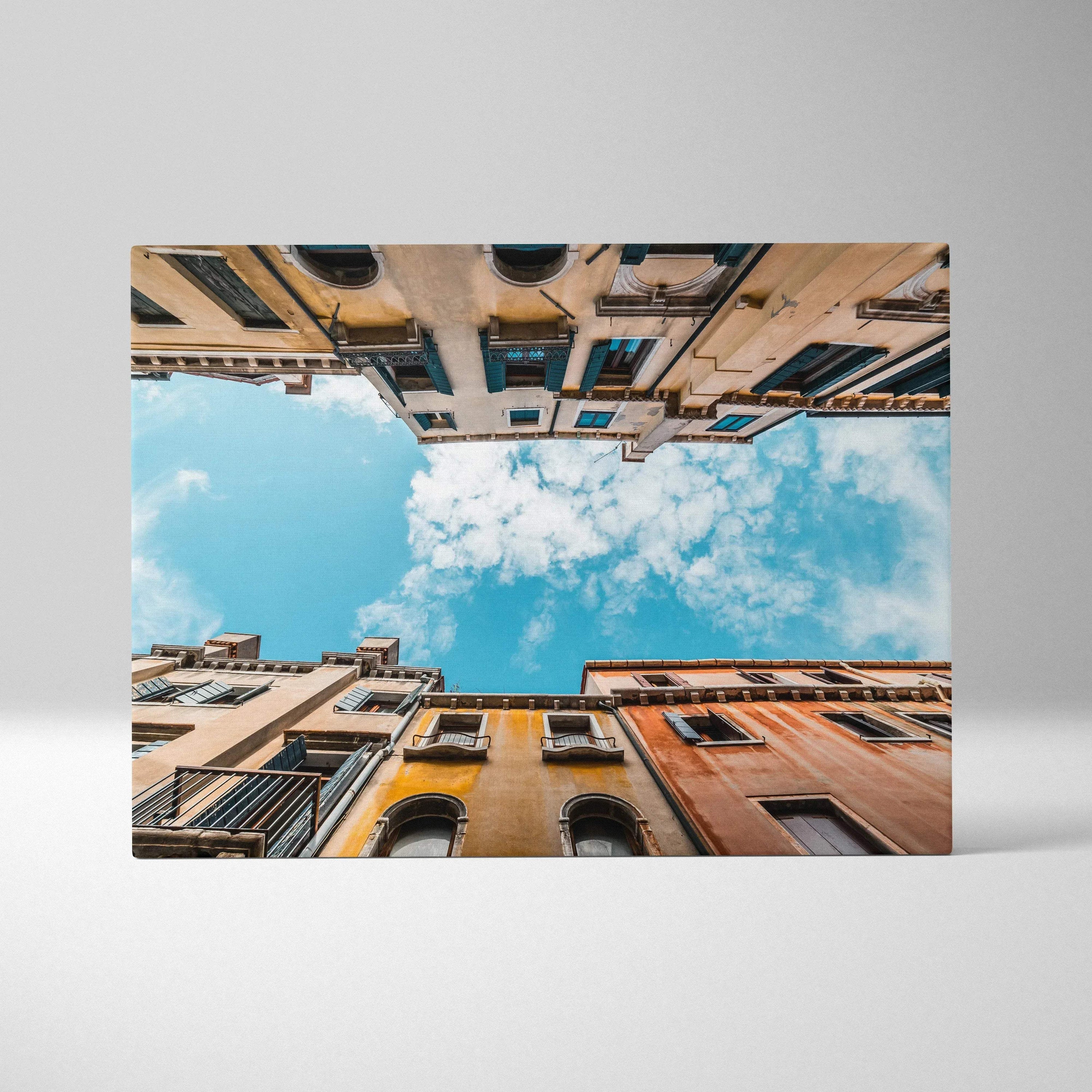Canvas wall art print showing upward view of colorful urban buildings framing a bright blue sky with clouds.