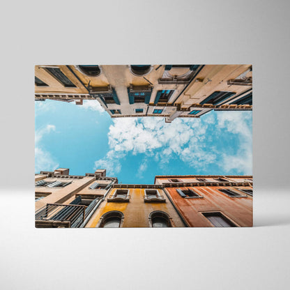 Canvas wall art print showing upward view of colorful urban buildings framing a bright blue sky with clouds.