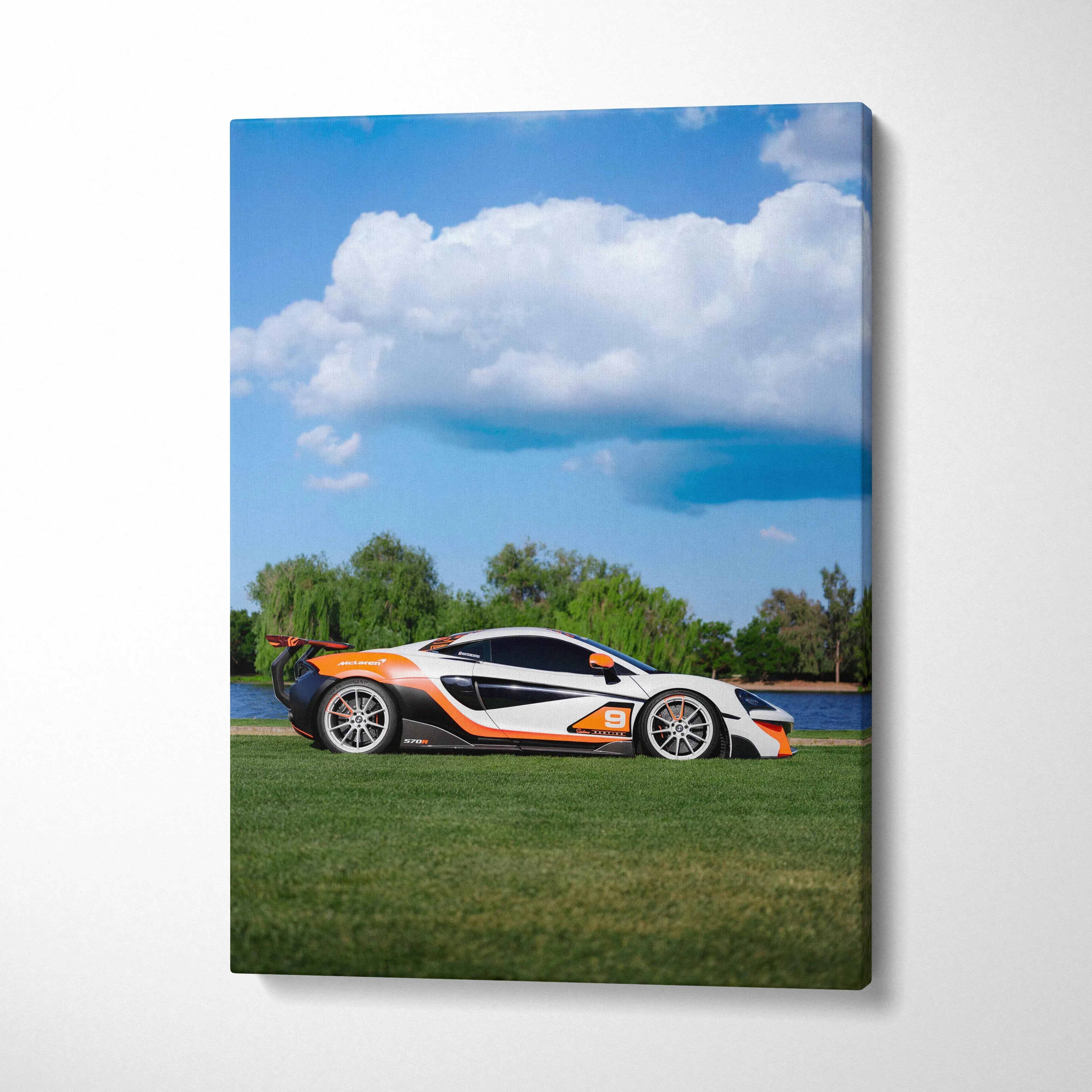 Vertical canvas wall art featuring a white and orange McLaren 570S sports car on green grass under a blue sky with clouds.