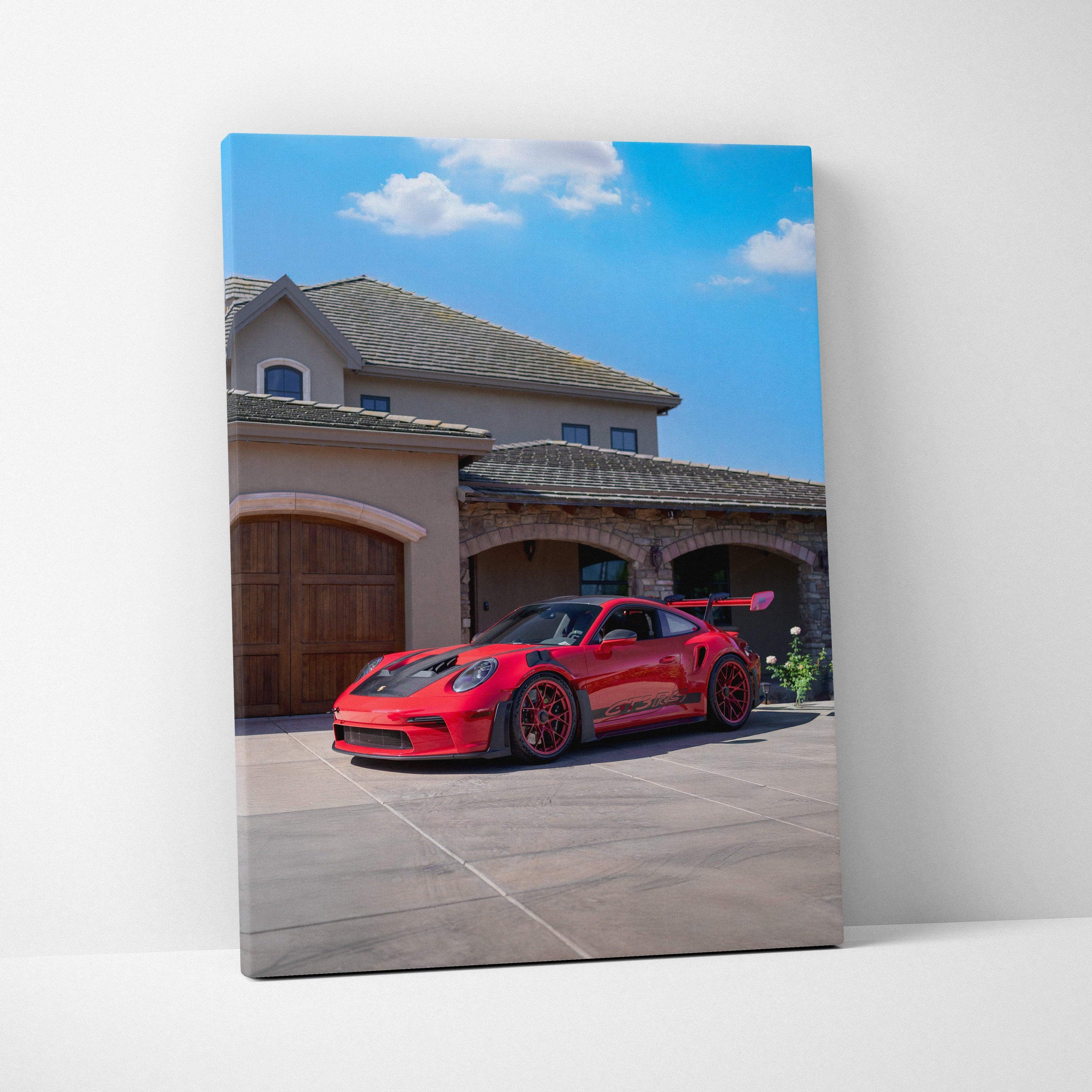 Vertical canvas art of a red Porsche 911 GT3 RS parked in front of a modern house under a blue sky.