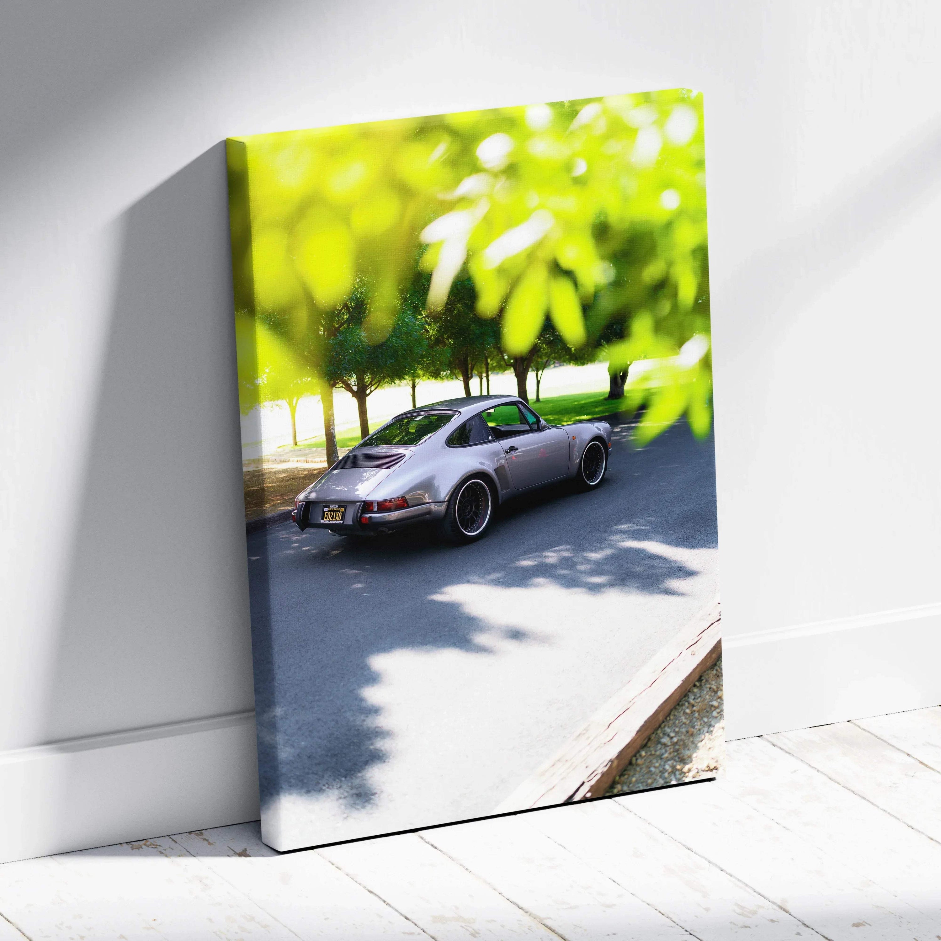Porsche 911 classic car with green tree canopy on vertical canvas wall art leaning on white floor.