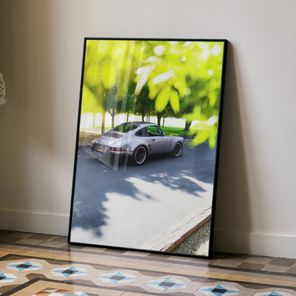 Porsche 911 classic car poster leaning against wall with green foliage reflection, modern wall art.
