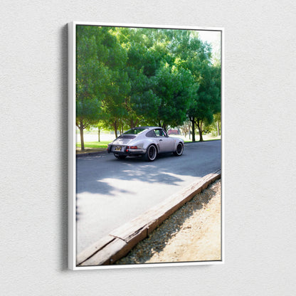 Vertical canvas art featuring a classic Porsche 911 driving past green trees as wall art.
