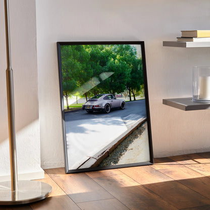 Porsche 911 classic car poster in black frame leaning against wall on wood floor wall art.