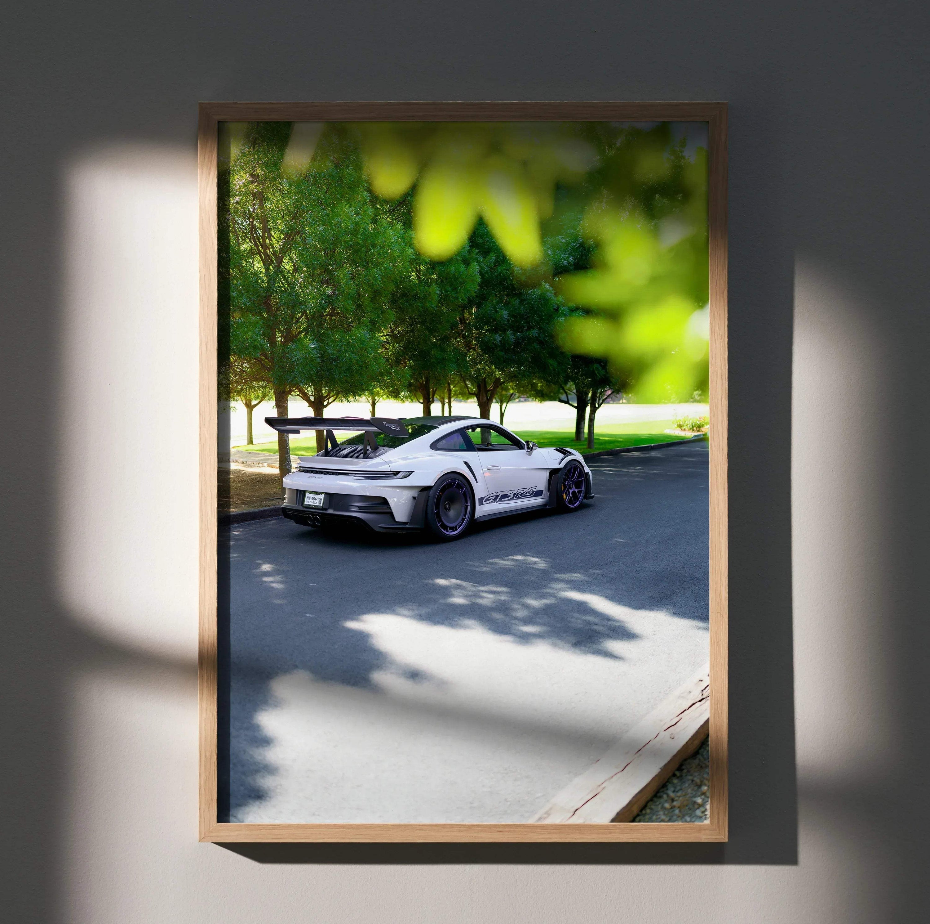 Porsche 911 GT3 RS poster showing white sports car on street with green trees, wall art in wooden frame.