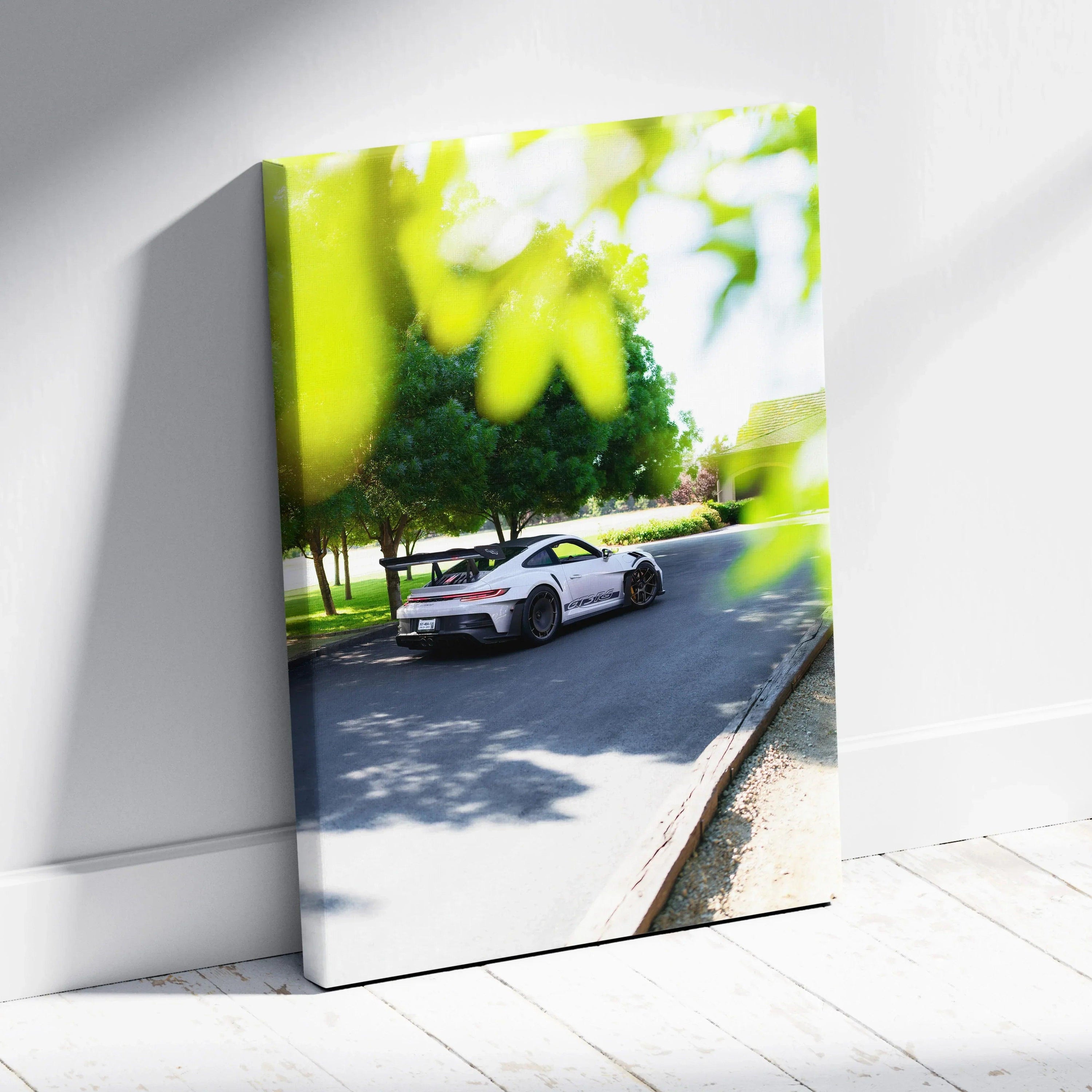 Vertical canvas wall art featuring a white Porsche 911 GT3 RS parked on a sunlit street with green trees.