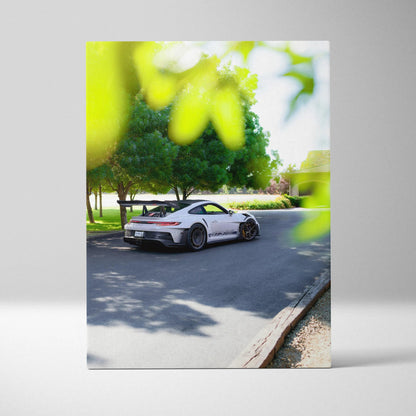Vertical canvas wall art of white Porsche 911 GT3 RS on sunlit road with green trees background.