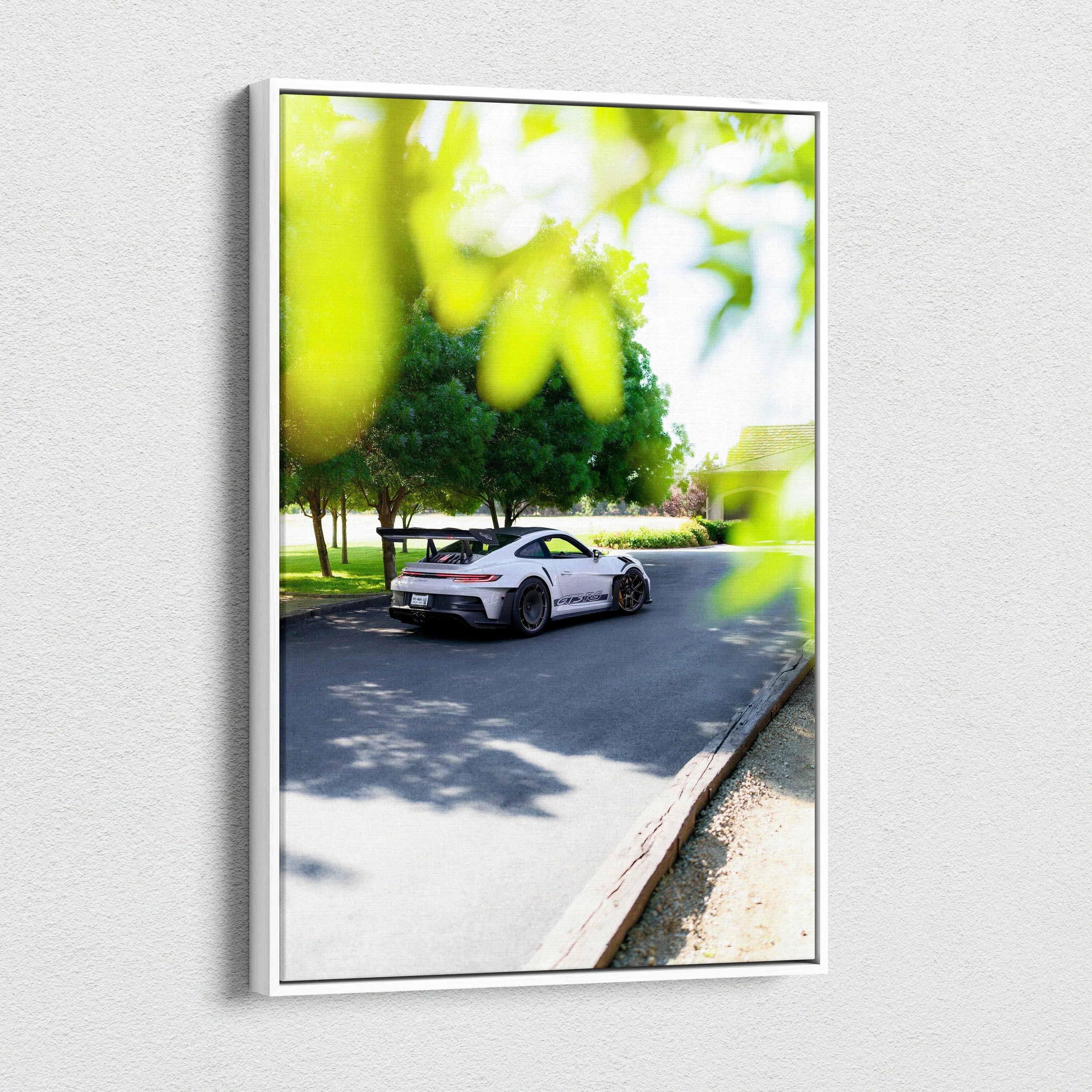 Vertical canvas art featuring a white Porsche 911 GT3 RS driving on a sunlit road with green foliage blurred in foreground.