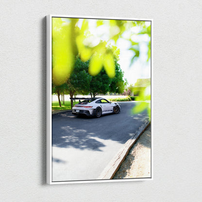 Vertical canvas art featuring a white Porsche 911 GT3 RS driving on a sunlit road with green foliage blurred in foreground.